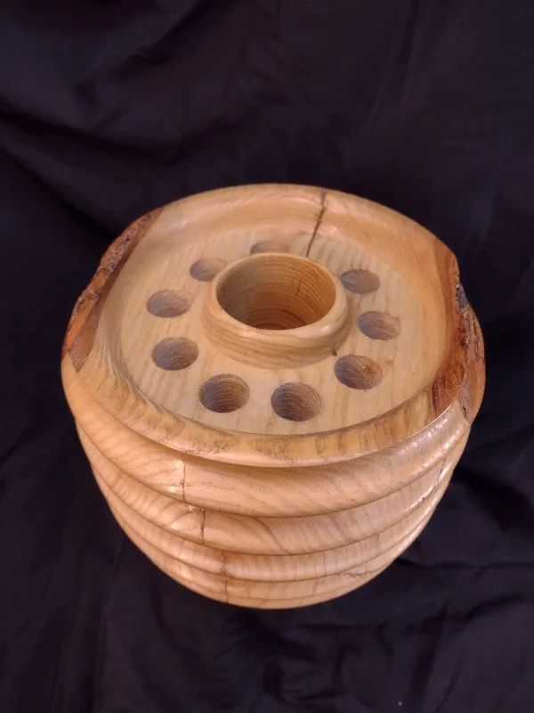 A wooden yarn swift with multiple holes on top for holding skeins of yarn, placed against a black fabric background.