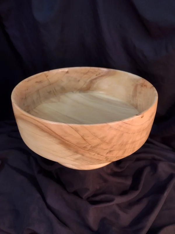 A round wooden bowl with a smooth, polished surface, resting on a dark fabric background.