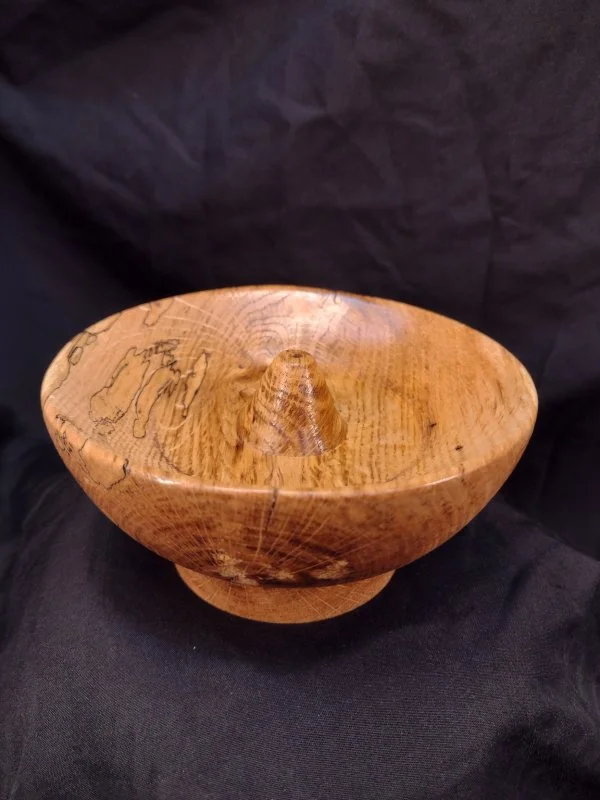 Wooden bowl with a rounded protrusion in the center, placed on black fabric background.