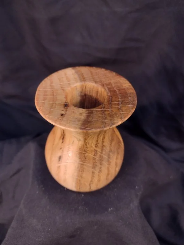Wooden vase with a round base and an open top, placed on a black fabric background.