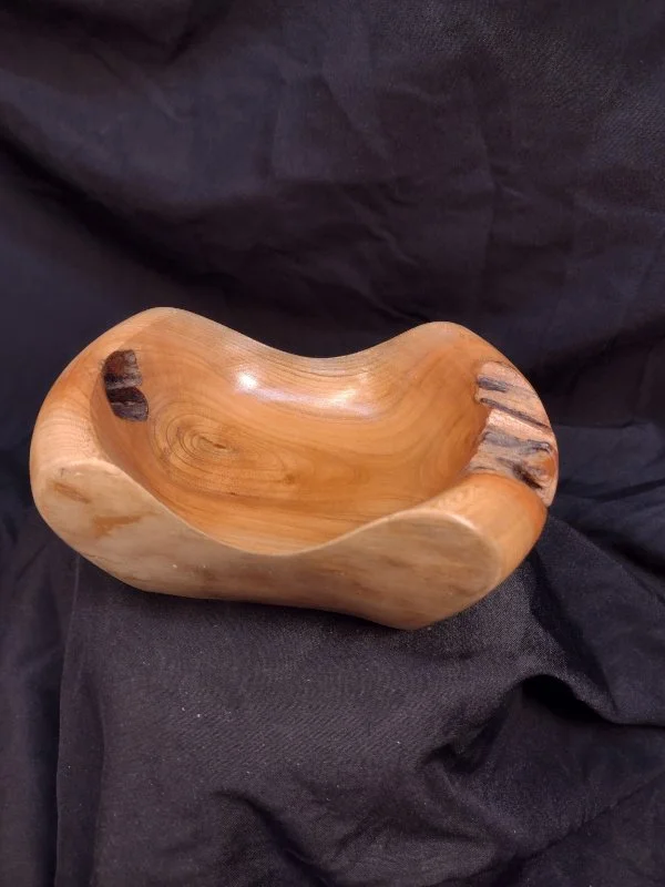 A wooden bowl with a smooth, polished interior and natural, uneven edges, placed on a black fabric background.