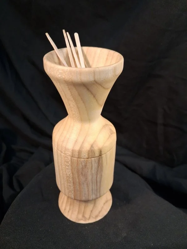 A wooden vase with several chopsticks inside, set against a dark background.