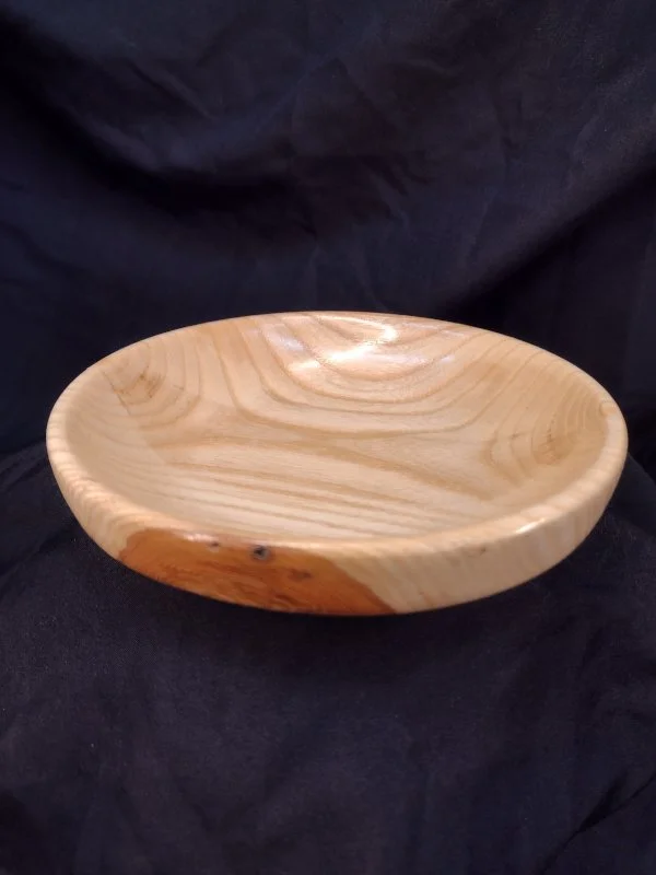 Wooden bowl with natural grain, placed on black fabric background.