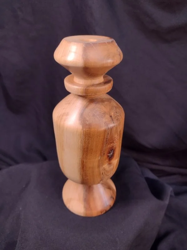A wooden sculpture with a rounded top, a narrow middle with a ring, and a rounded base, carved from a piece of wood with visible grain patterns.