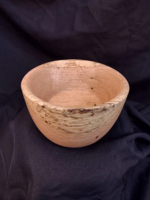 A wooden bowl with a natural finish, sitting on a black fabric background.