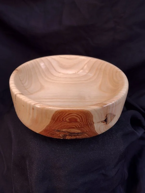 A wooden bowl with a smooth, polished finish and natural wood grain pattern sitting on a black fabric background.