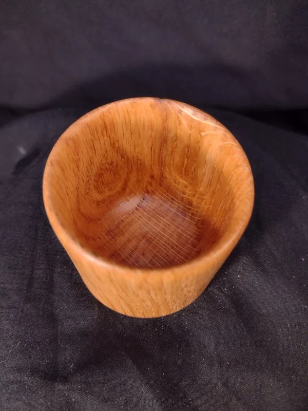 A small wooden bowl with a polished surface, sitting on a black fabric background.