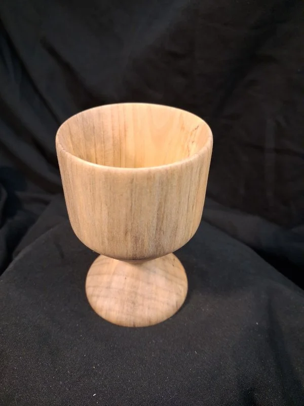 A wooden goblet with a smooth, polished finish, placed on a black fabric background.