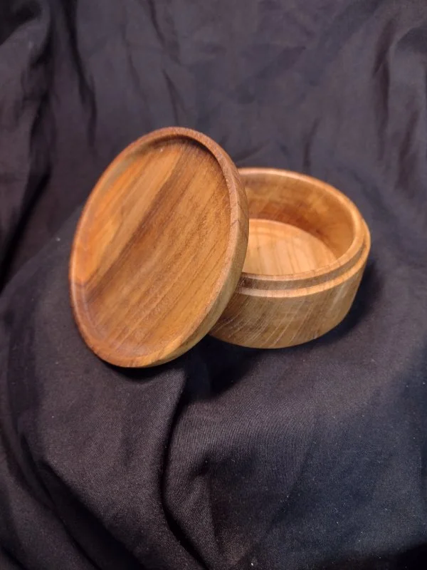 Wooden round container with lid on a black fabric background.