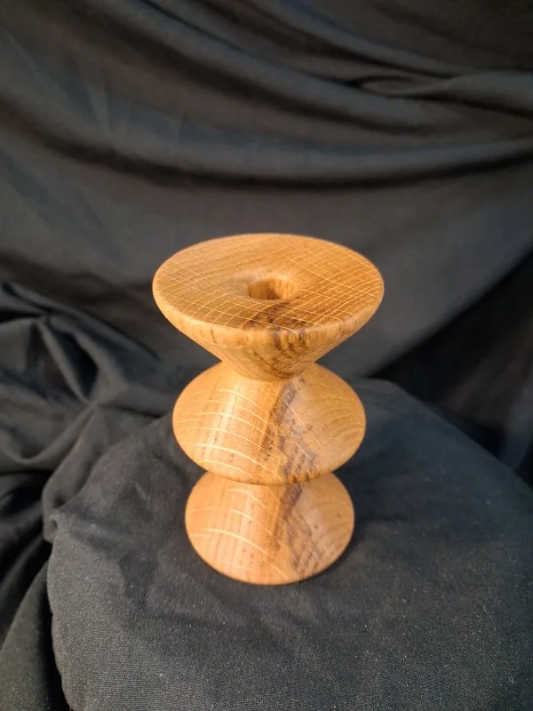 A wooden spinning top toy with a rounded top and base, placed on a black fabric surface.