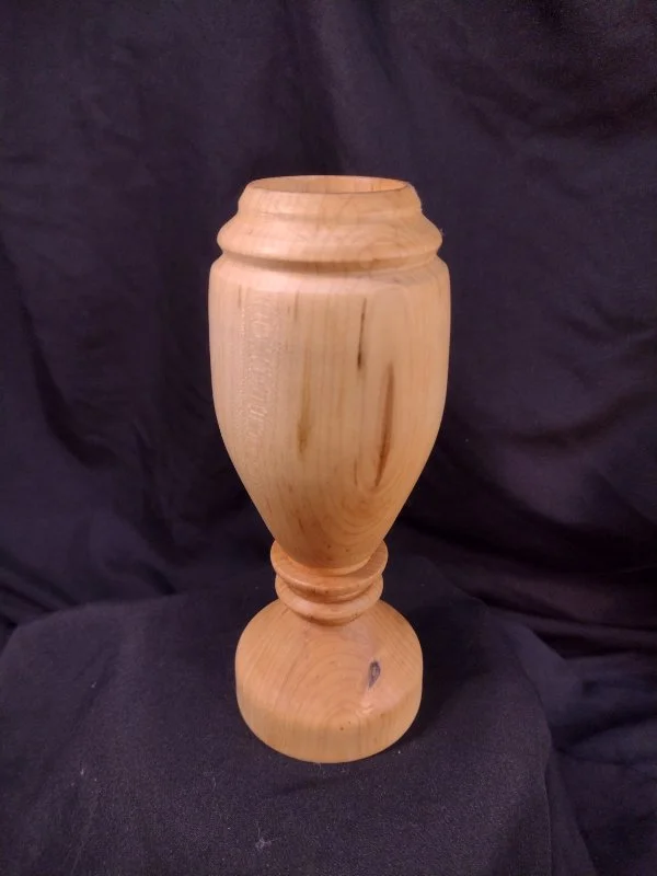 Unfinished wooden vase with carved decorative details, placed on a black fabric background.