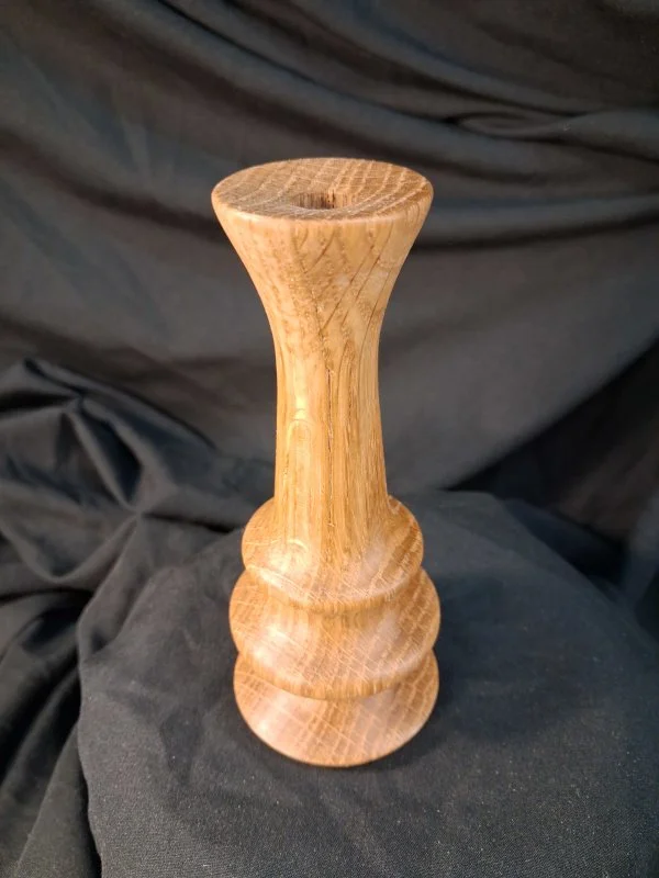A wooden carving with a turned design, standing upright on a black fabric surface.
