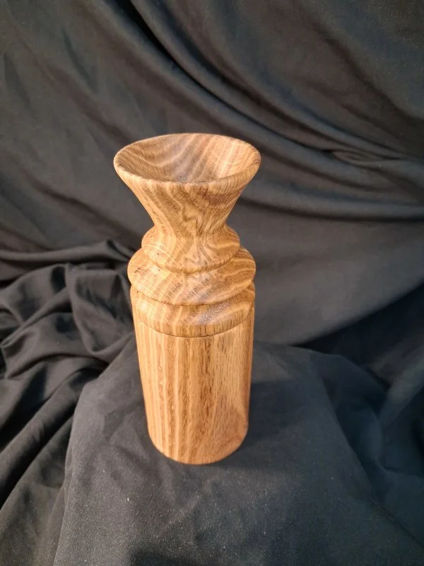 A wooden pestle or grinding tool with a smooth, rounded top, placed on a dark fabric background.