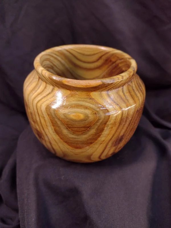 A wooden bowl with visible wood grain, placed on dark fabric.