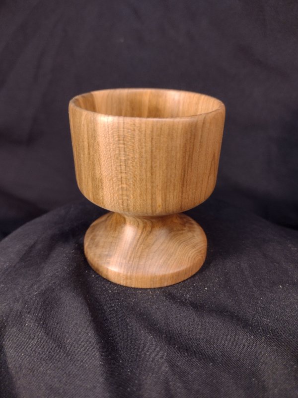 A wooden goblet with a rounded base and a cup-shaped top placed on a black fabric background.