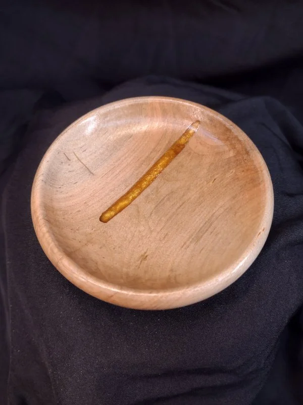 A wooden bowl with a partially burned cigarette inside, resting on black fabric.