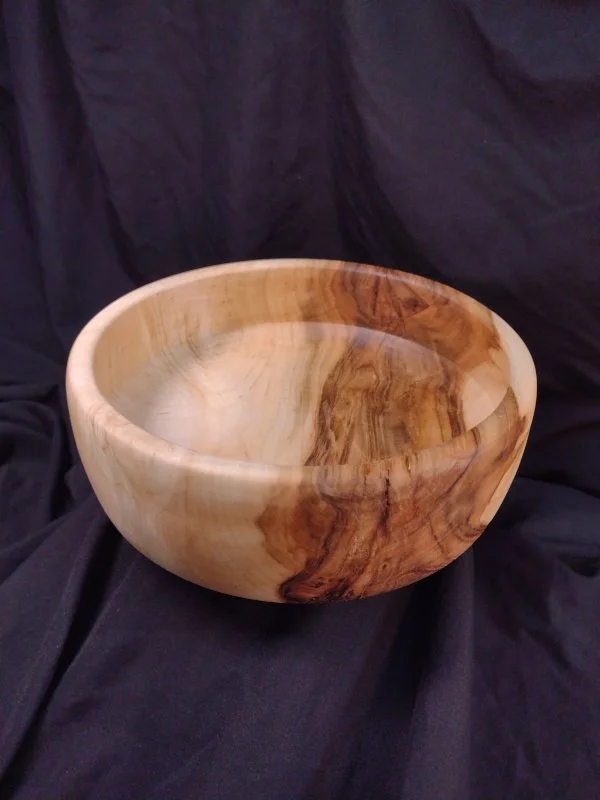 A wooden bowl with a smooth finish, showing natural wood grain patterns, placed on a black fabric background.
