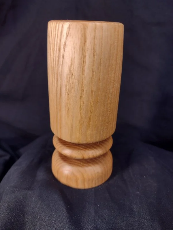 A tall, wooden vase with a rounded base, placed on a dark fabric background.