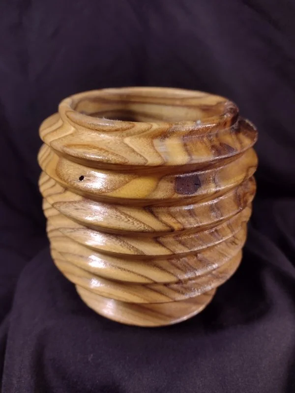 Wooden carved vessel with a spiral, layered design against a dark background.