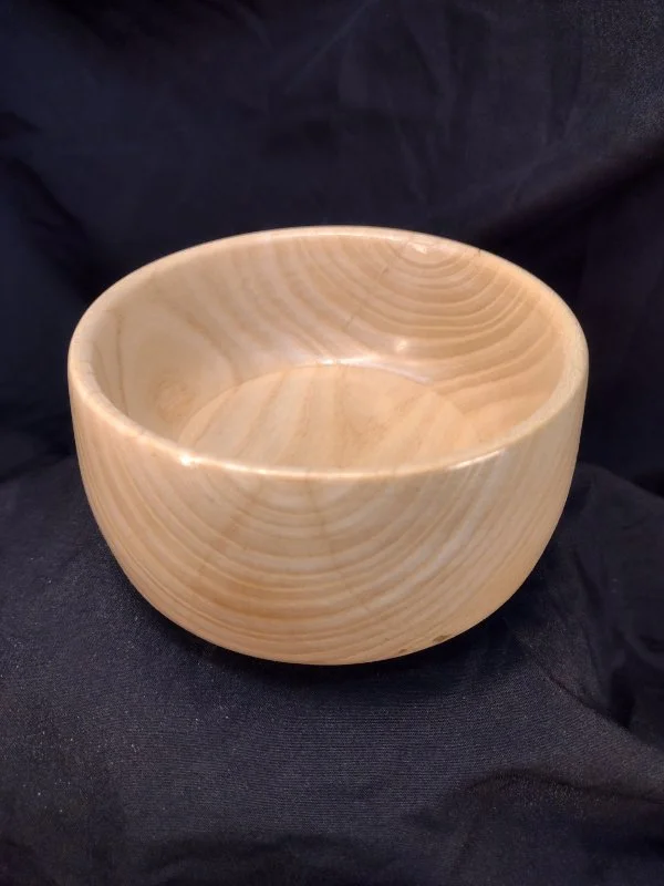 A round, wooden bowl with a smooth, polished surface, sitting on a dark fabric background.