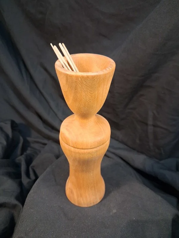 A tall wooden mortar and pestle with chopsticks placed inside the mortar.