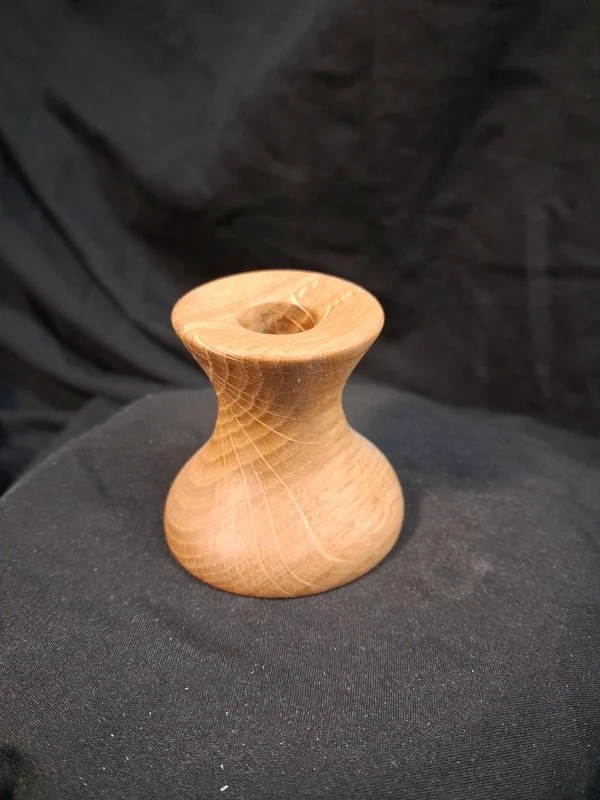 A small wooden object with a rounded, hourglass shape and a hollow center, sitting on a black fabric surface.