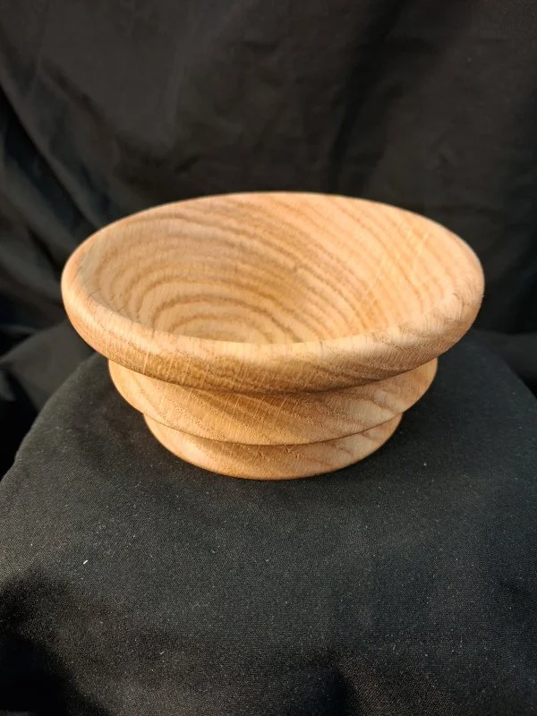 A small, round wooden bowl with a smooth, polished surface resting on a black fabric background.