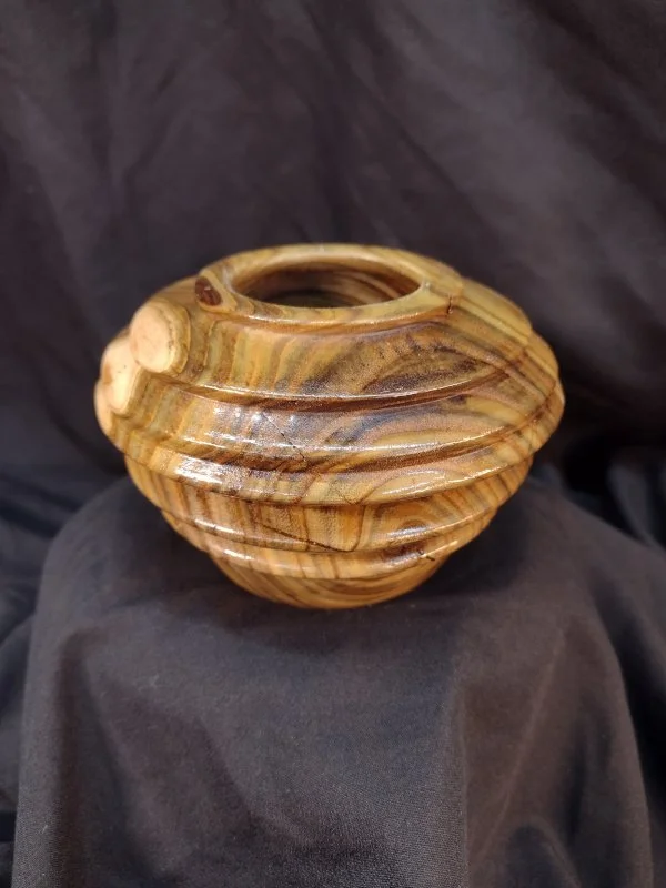 Wooden decorative vase with a rounded, layered design and a small opening at the top, placed on black fabric.
