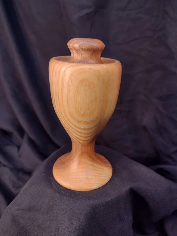 Wooden urn with a rounded top, central hole and elongated body.