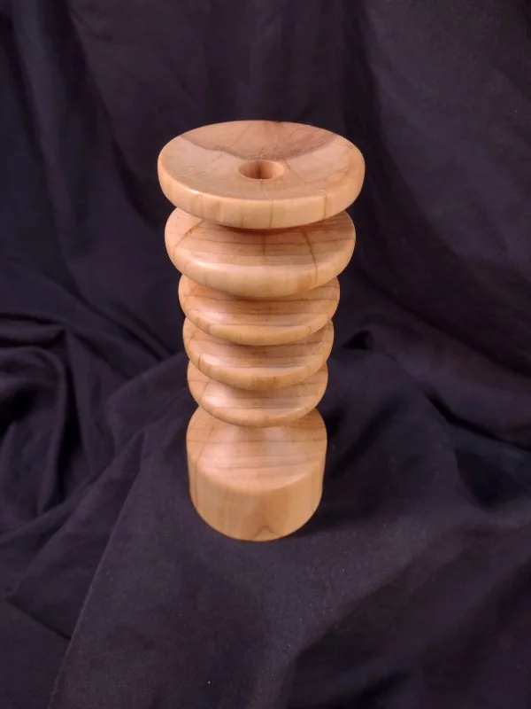 A wooden sculpture with multiple stacked, rounded discs, ending with a broader base, set against a dark fabric background.