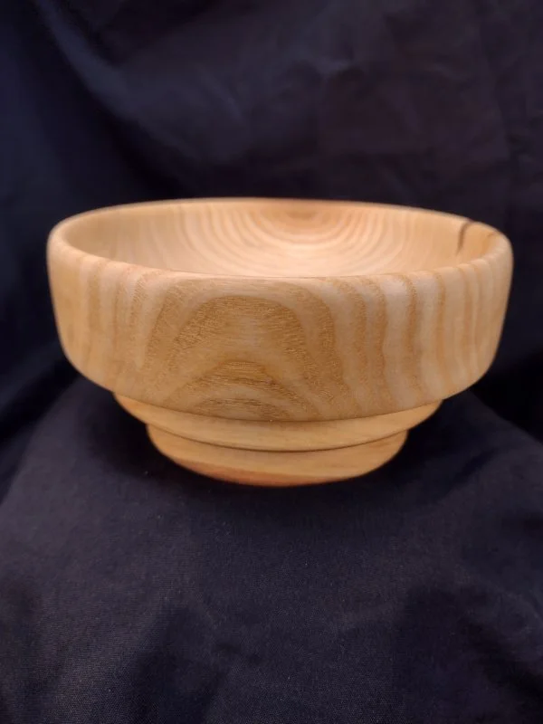 A wooden bowl with a smooth, polished surface resting on a black fabric background.
