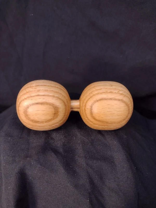 A wooden massage roller with two large, rounded sections connected by a short handle, placed on a dark fabric background.