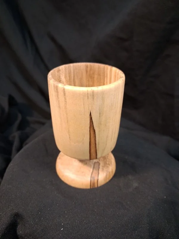 Wooden cup with a small base on a dark fabric surface.