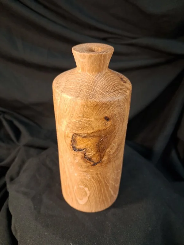 Wooden vase with a natural finish and visible wood grain, placed on a black surface.