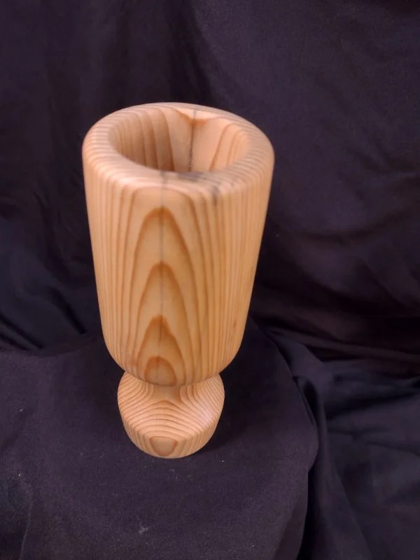 A tall, wooden decorative vase with a natural wood grain pattern on a black fabric backdrop.