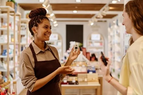 A smiling store clerk showing a small product to a customer in a retail store.
