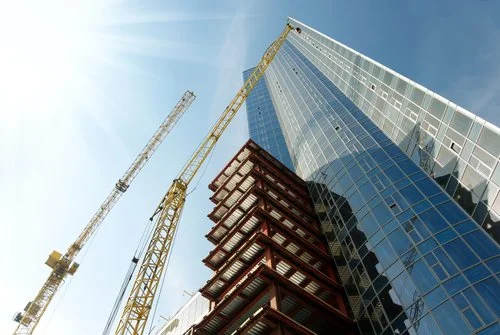 Under construction high-rise building with cranes and scaffolding against a clear sky.