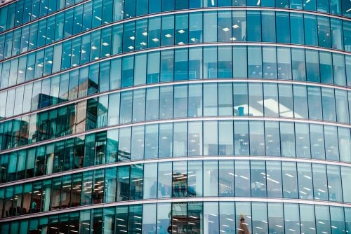 Close-up of a modern glass office building with curved windows and reflections of surrounding buildings.