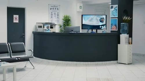Hospital reception area with a curved black counter, computer monitor, water dispenser, and seating.