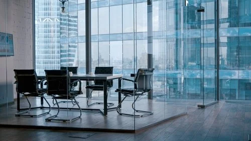 Modern office conference room with a glass wall and cityscape view, featuring a table and six chairs.