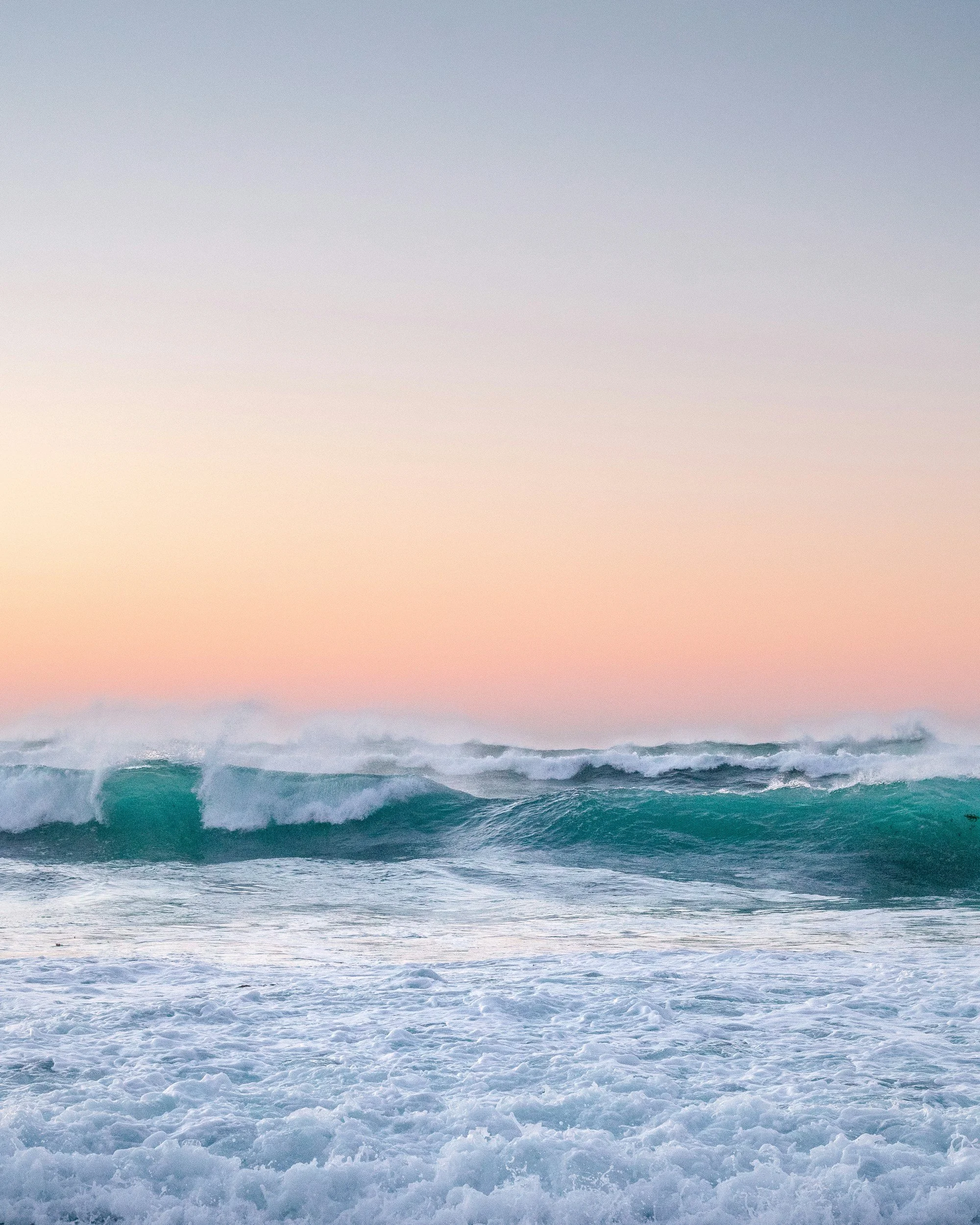 Ocean waves crashing at sunset with a pink and light blue sky