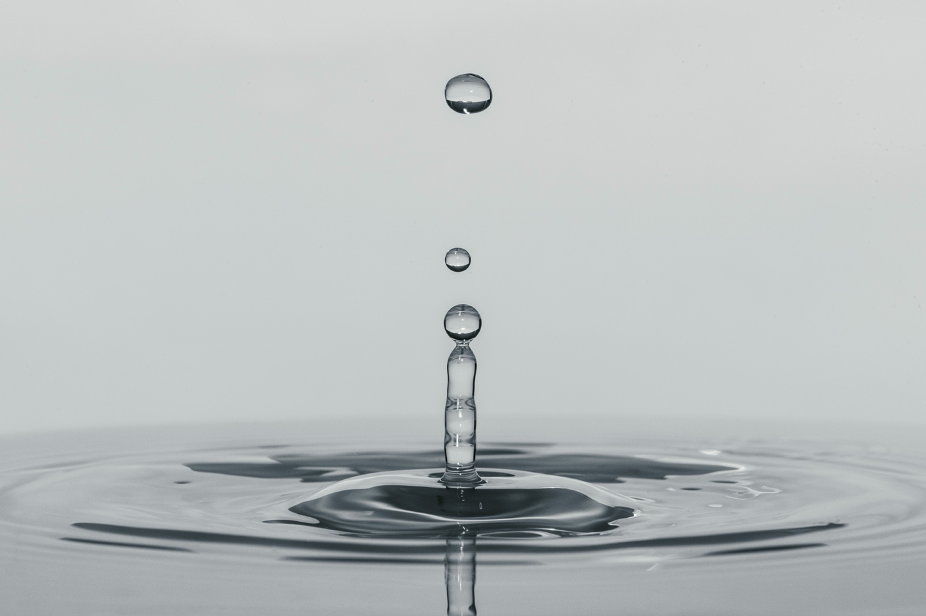 Close-up of water droplets falling into a still water surface, creating ripples. Showing how small changes have ripple effects in mental health.