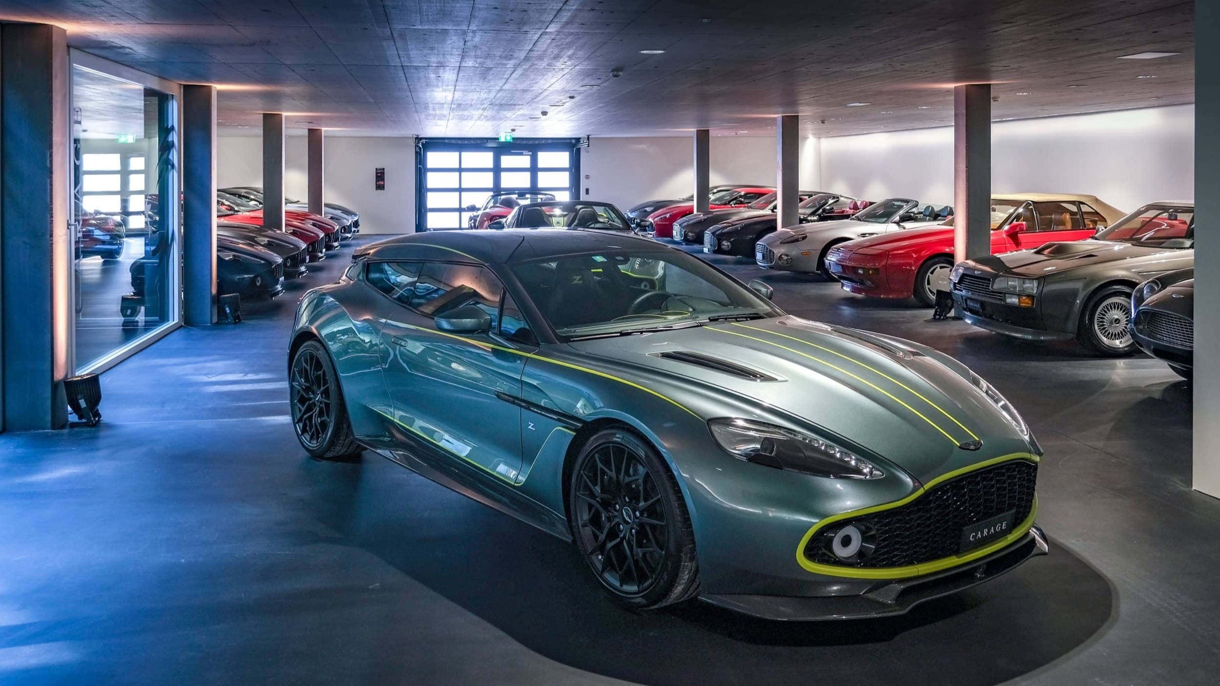A modern garage filled with a variety of luxury and sports cars, with a green sports car in the foreground and more cars in the background.