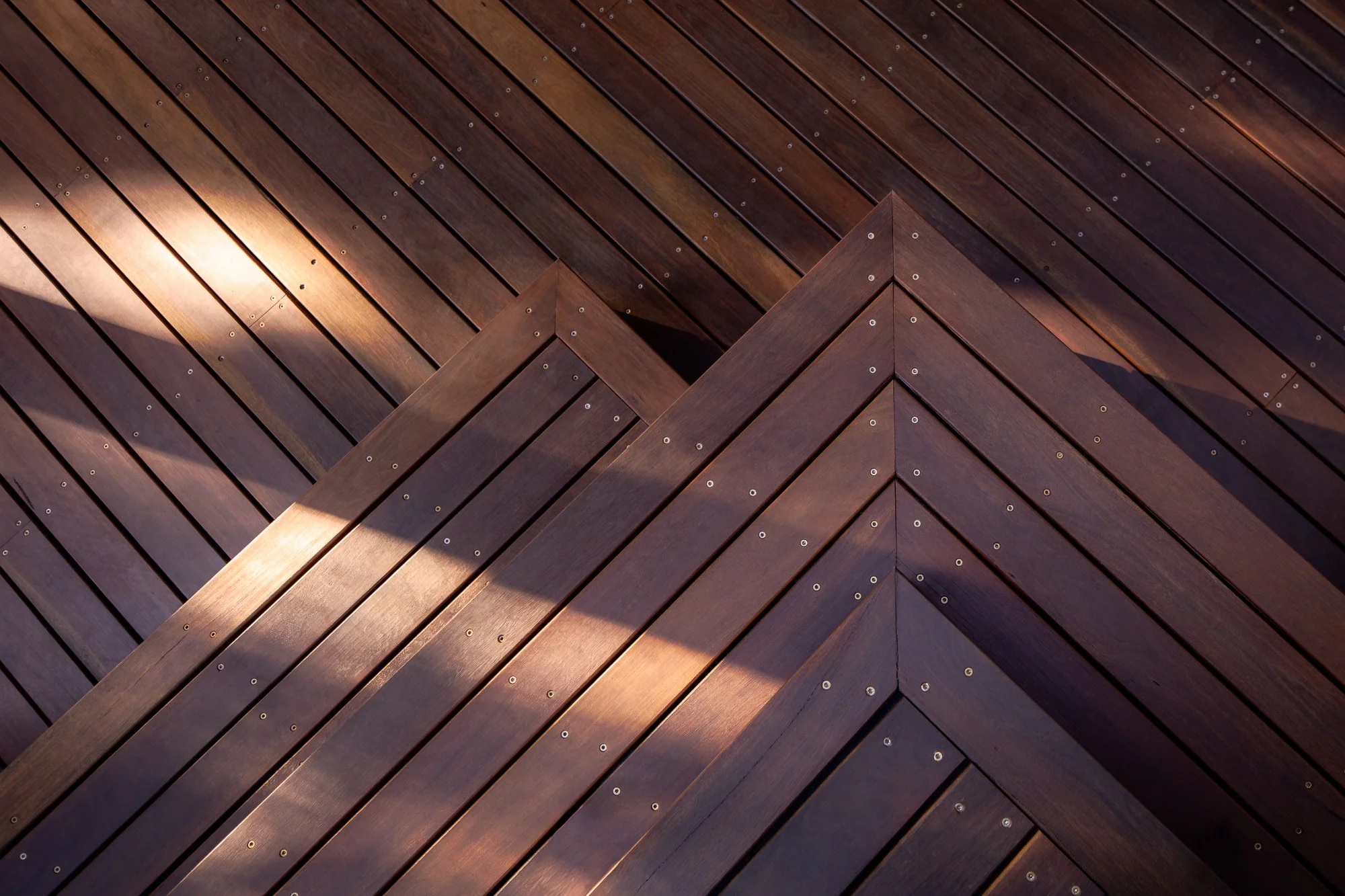 Close-up of a wooden corner with diagonal planks and visible screws, showing sunlight reflecting on the surface.