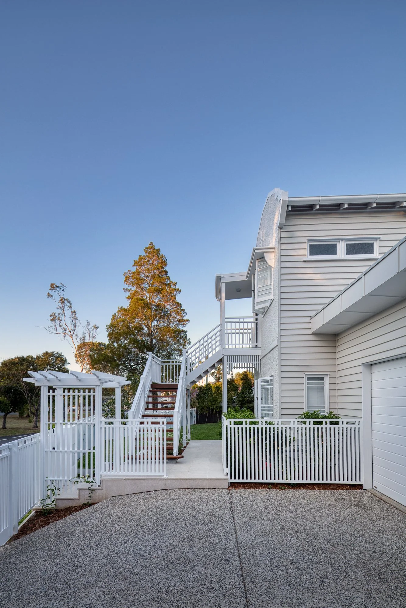 A white house with a staircase leading up to a second-story porch, surrounded by a white fence. 