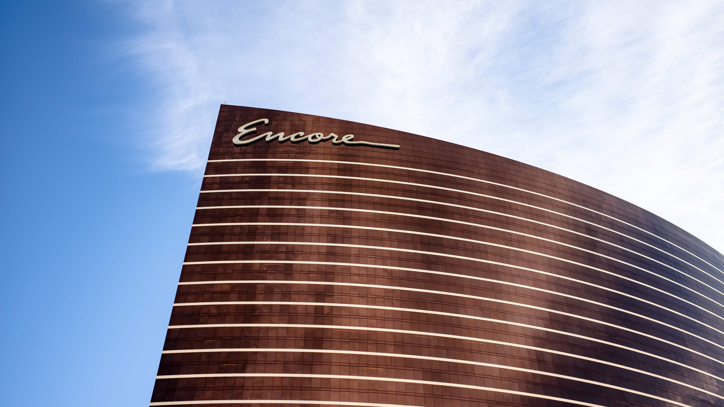A tall, curved building with the word 'Encore' written in white cursive at the top, against a background of a partly cloudy blue sky.