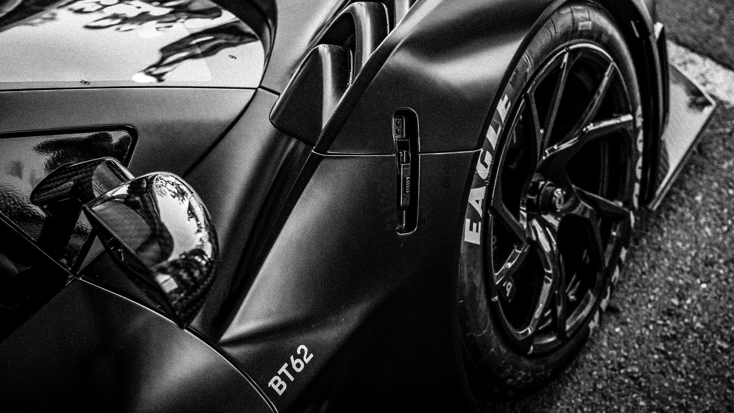 Close-up of a sleek, black race car focusing on the front left corner, including the headlight, part of the hood, and the wheel with a racing tire displaying "EATCAR" branding.
