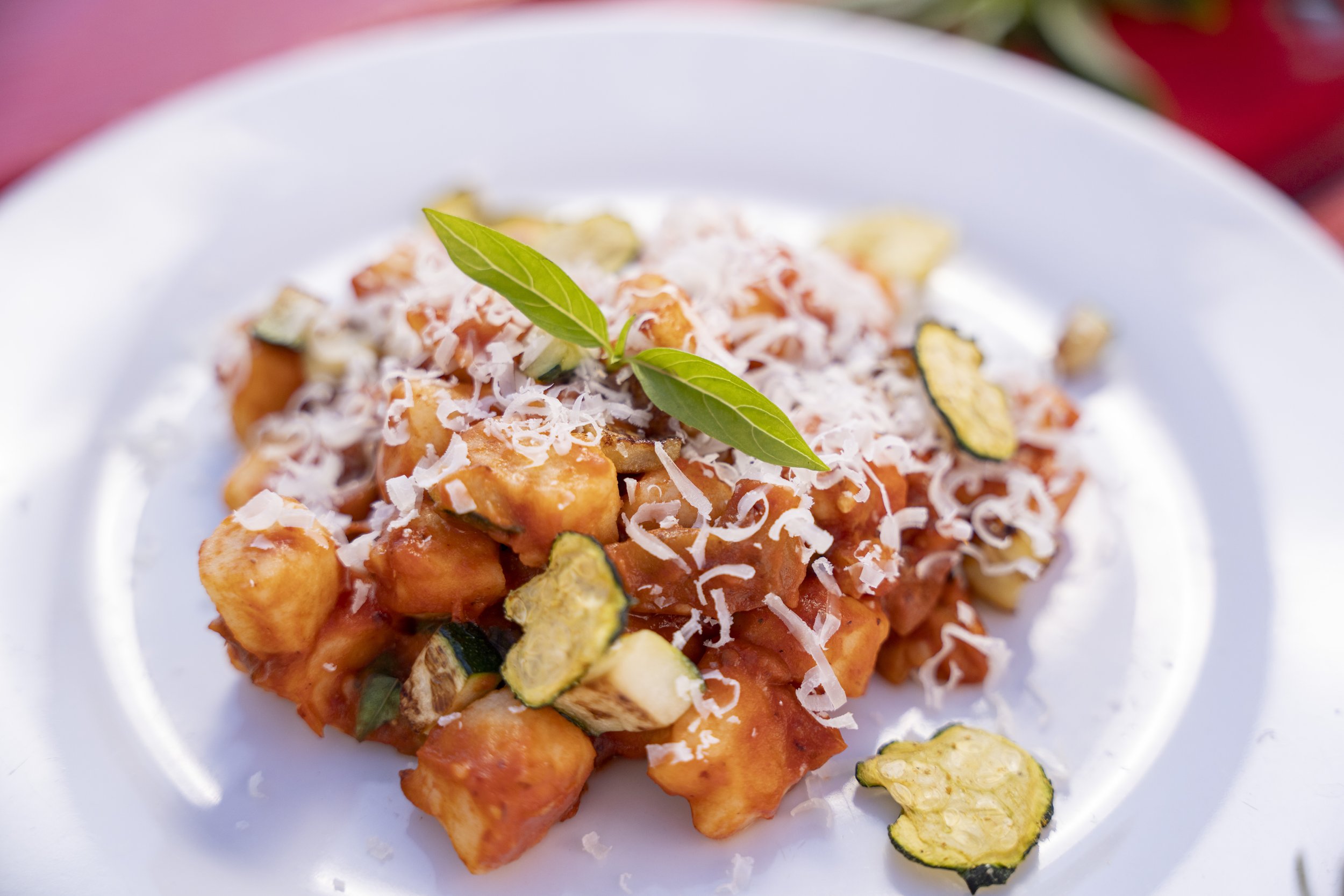 Close-up of a plate of gnocchi pasta topped with tomato sauce, grated cheese, and garnished with basil and zucchini slices.