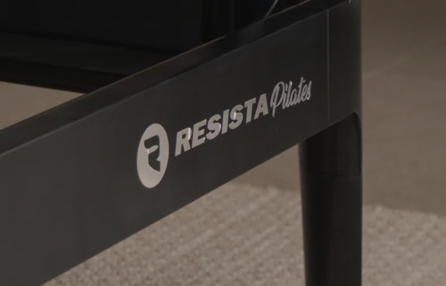 Close-up of a black fitness equipment with the brand name 'RESISTA Pilates' printed on it.