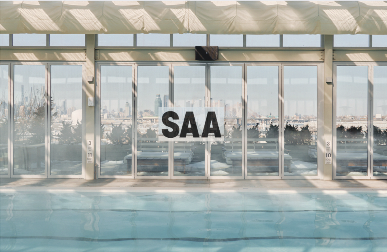 Indoor swimming pool with glass windows and city skyline view, sign reading 'SAA' in the center of the window.